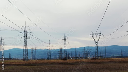High voltage transmission towers and power lines cross a rural landscape during daylight.