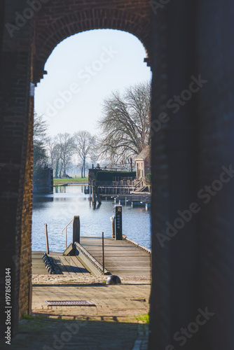 Quiet waters reflect bare trees through an ancient archway.