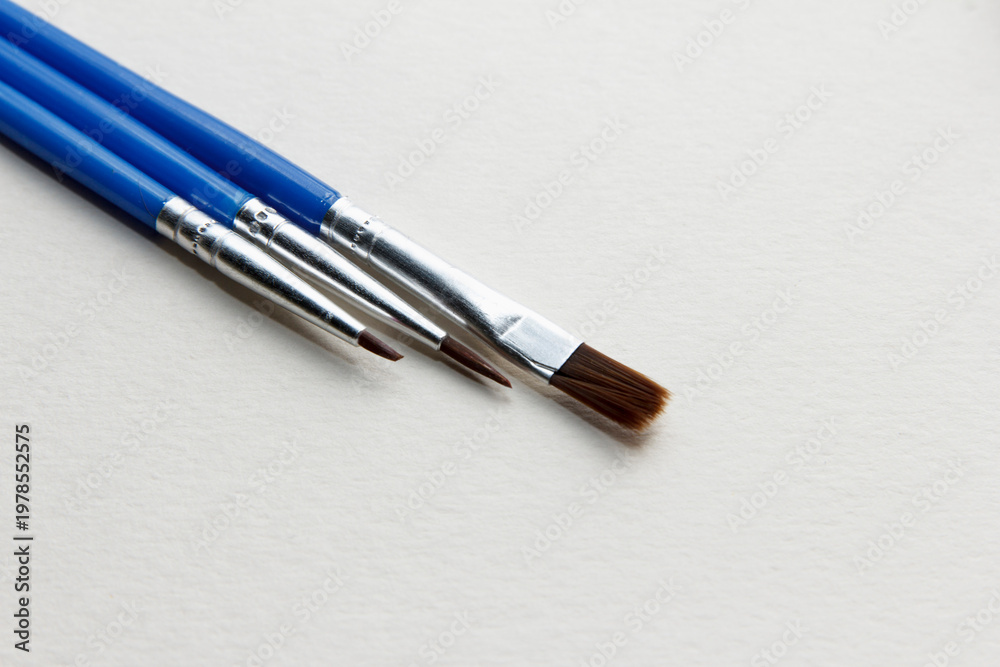 Fototapeta premium Three paintbrushes with blue handles arranged on a blank canvas