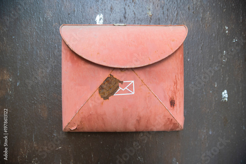 Fotografie Old red metal mailbox shaped like an envelope mounted on a dark wall