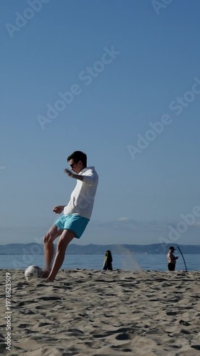 Man playing football on beach at sunrise, outdoor sports activity.