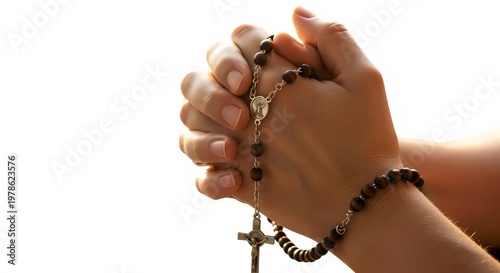 Holy Christian image of rosary beads wrapped around praying hands illuminated by warm rays captured in premium isolated studio composition