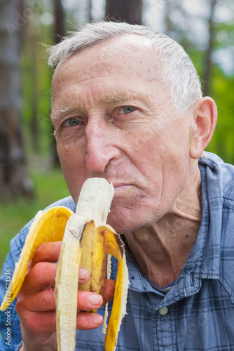 An elderly man eats a ripe banana