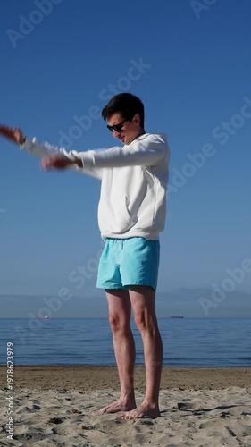 Man doing relaxing stretch on beach at sunrise, light morning workout.
