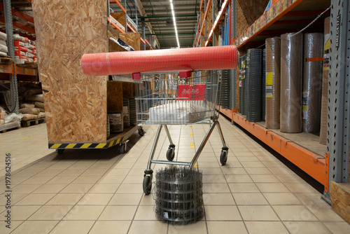 Shopping cart with red roll on top and wire bundle in store aisle during daytime