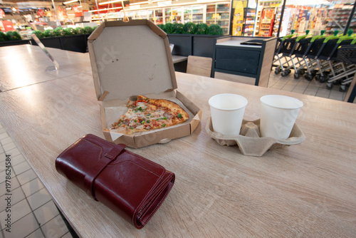Pizza box with leftover slice and two drink cups placed on a wooden table in a store