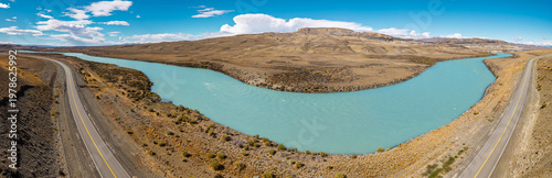 Aerial panoramic view of the turquoise Santa Cruz River winding through the dry desert landscape of Patagonia, Argentina, with a scenic road alongside.