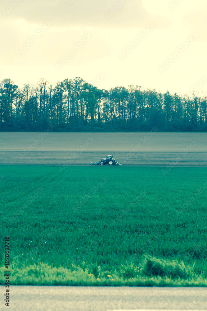 Fototapeta premium Blue-Toned Tractor Plowing a Field