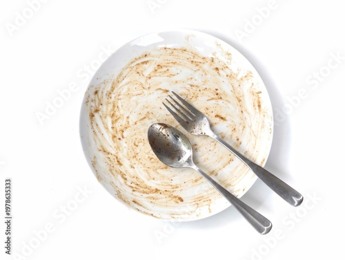 Dirty empty white plate after meal with spoon and fork isolated on white background. perfect for themes of food waste, hunger, finished dinner, or dishwashing concepts