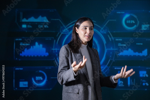 Professional woman in a grey blazer presenting data insights with a digital dashboard of graphs and charts in the background, conveying a tech and analytics theme.