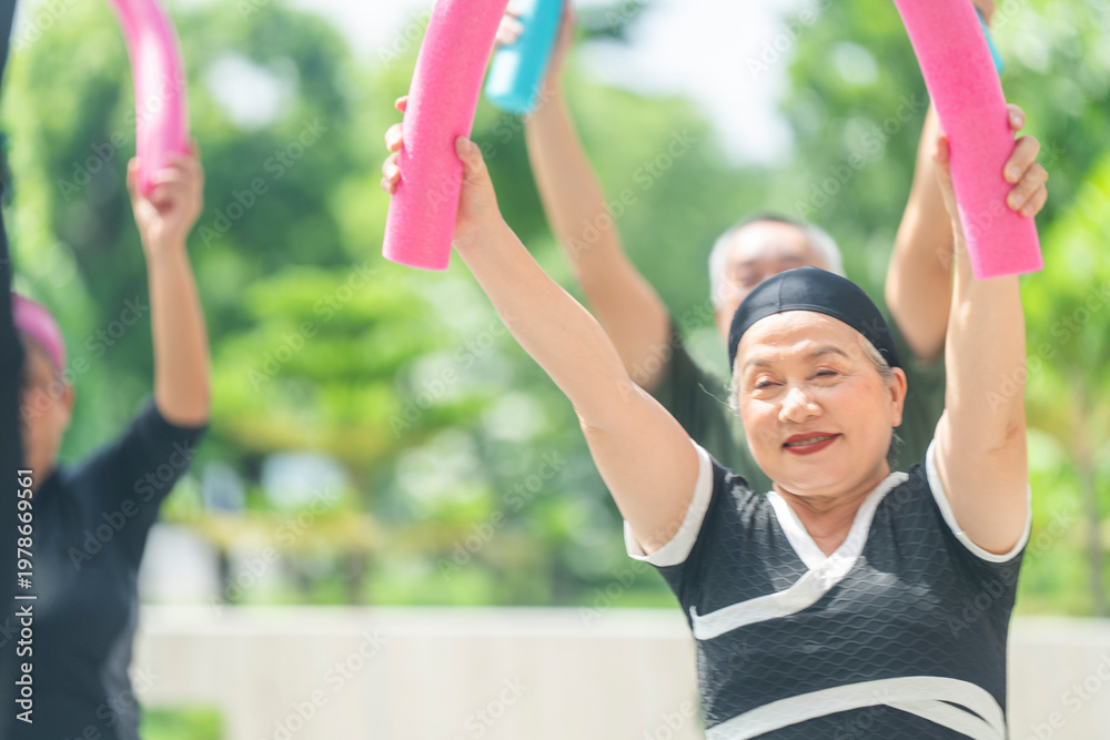 Obraz premium Portrait of happy mature woman using a foam noodle for fitness training. Joyful senior friends exercising together to maintain good health and wellbeing.
