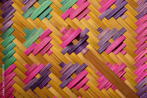 Macro of colorful dyed bamboo wickerwork with intricate geometric pattern. Traditional Thai handicraft texture in pink, purple, and green.