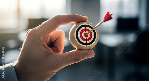 Hand holding small dartboard with arrow in bullseye, close-up, success and goal achievement