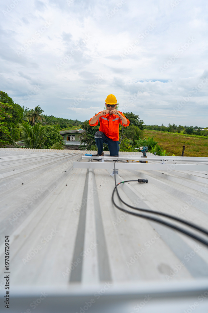 Obraz premium Technician in safety uniform and helmet kneeling on a rooftop, using a drill for precise installation work. A scene highlighting safety, professionalism, and technical expertise in construction.