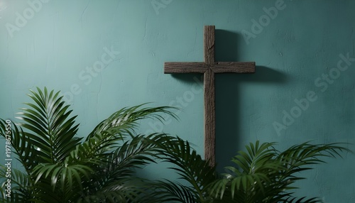 A simple wooden cross stands against a teal wall, surrounded by lush green leaves, symbol of faith