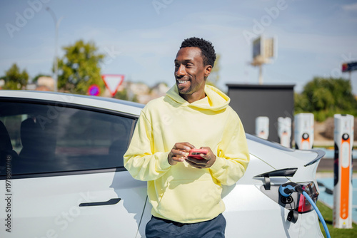 Young black man charging electric car with smartphone