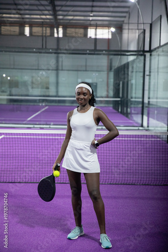 African American woman mid-30s white-dress posing on purple court balancing yellow ball on racket