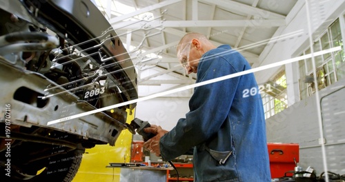 Grinding bald mechanic in blue coverall fixing front chassis at garage, with grinder and timeline
