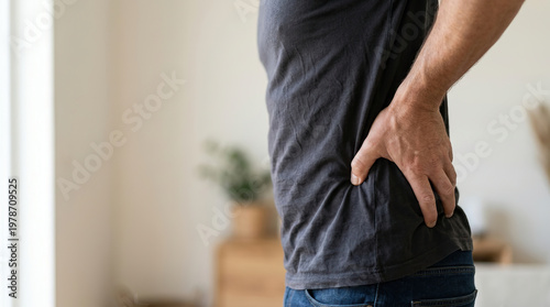 Back pain man hand hip waist injury discomfort home health lifestyle male adult backache muscle spine posture chronic ache tension fatigue stress indoors casual clothing jeans t shirt torso side