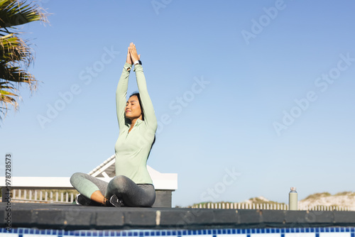 Tablou pe pânză Mid-adult Asian woman sitting crosslegged on pool ledge meditating by blue tiles