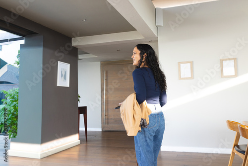 Woman standing by wooden front door looking back holding beige jacket and keychain, copy space