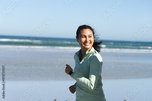 Konstfotografi Mid Adult Asian woman jogging along wet shore wearing light green zip-up and sma