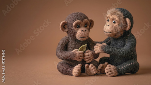 Needle felted wool sculpture of two baby chimpanzees, one holding a leaf, against a brown background. Handmade textile art showing soft plush monkey crafts.