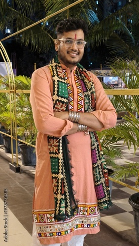 Indian man in traditional Navratri outfit for playing garba, wearing kurta with embroidered stole and tilak, posing outdoors with festive cultural style.