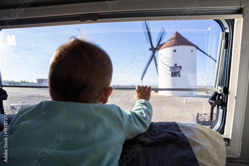 Baby looking at historic Spanish windmill from camper van