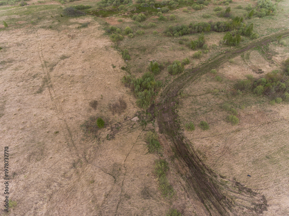 Fototapeta premium Aerial view of a dirt path winding through dry grass and sparse shrubs