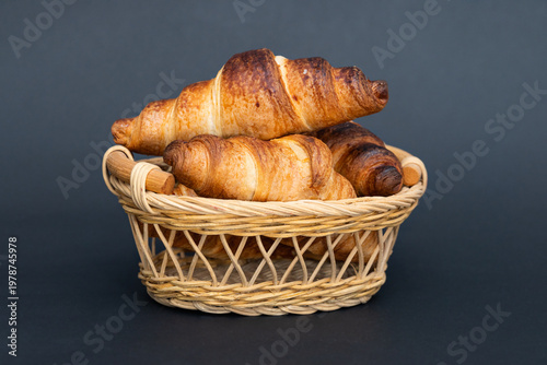 Freshly baked croissants in wicker basket close up on black background