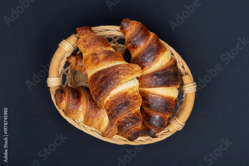 Freshly baked croissants in wicker basket close up on black background. View above
