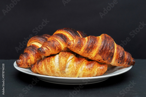 Freshly baked croissants on plate close up on black background