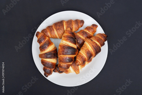 Freshly baked croissants on plate close up on black background. View above