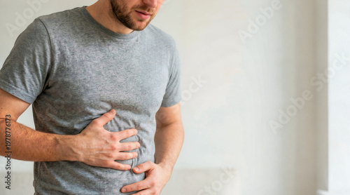 Man holding his stomach in pain. Adult male rubbing belly experiencing indigestion or nausea. Healthcare and medical concept. Copy space for text