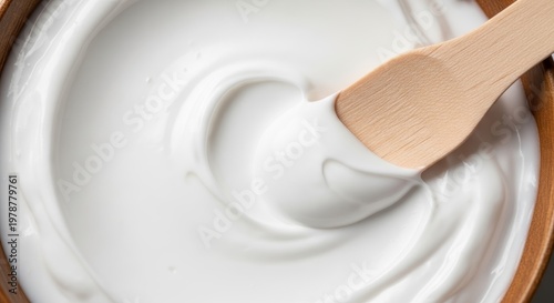 Creamy White Yogurt Swirled in a Bowl with a Wooden Spoon.
