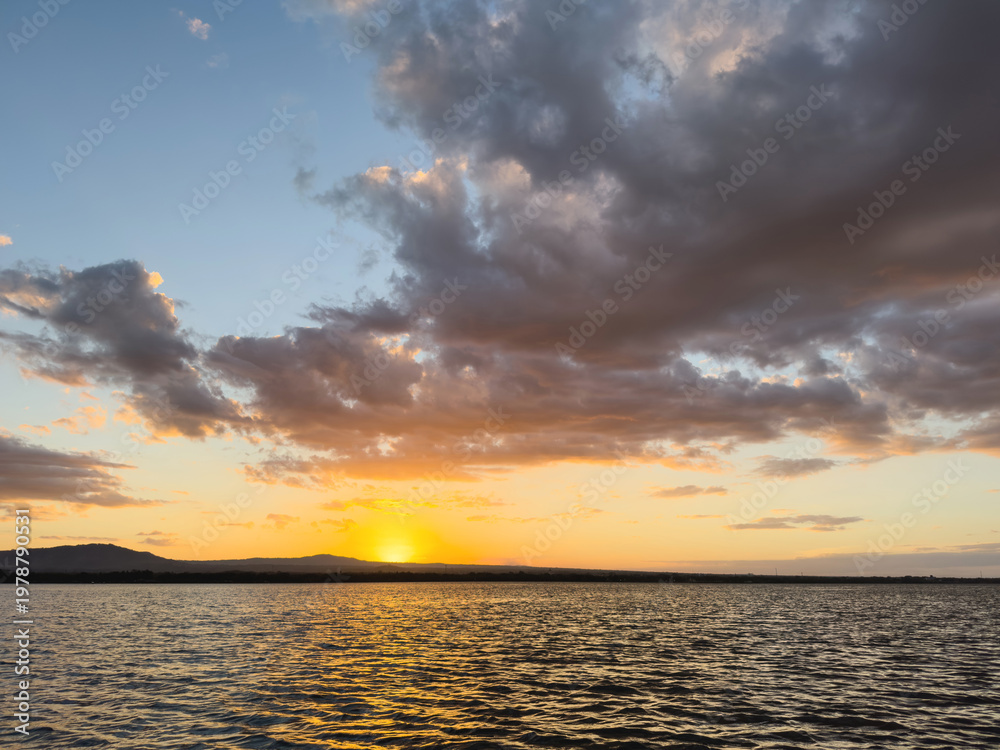 Obraz premium Sunset over a lake with clouds and mountains in the background