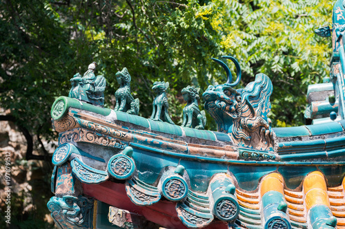Intricate green-glazed mythical figures line the ridge of a traditional tiled roof at Beijing's Summer Palace against a backdrop of lush greenery.
