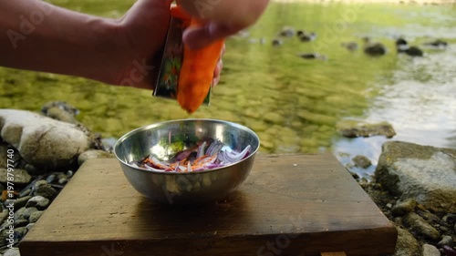Closeup of male hands grating fresh carrots near wild river at summer time. Cooking healthy food in outdoors. Camping food concept