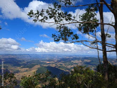 Expansive mountainous landscape with lush green valleys under a vibrant blue sky dotted with white clouds.