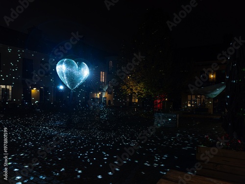 Glowing heart shaped disco ball casting bright reflections upon a dark quiet outdoor public urban square