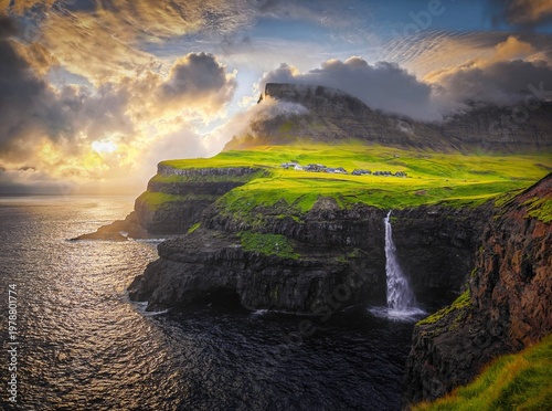 Dramatic waterfall flows over steep cliffs into the dark ocean under a beautiful golden sunset sky