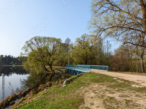 Blue metal bridge spanning across a calm river during a sunny spring day in nature