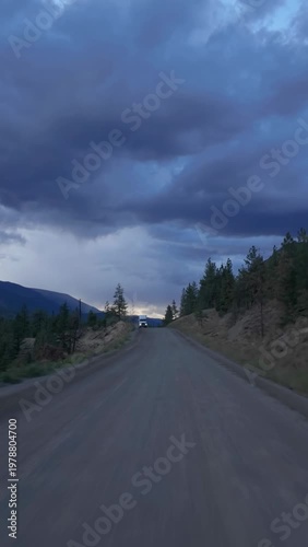 Heavy Haul Truck Drives on Remote Dirt Road Through British Columbia Mountains Under Dramatic Sky