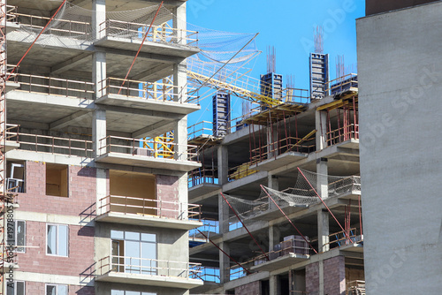 Modern building structures under construction, concrete frames forming new high rise residential or commercial developments against a bright blue sky, showing urban expansion and growth