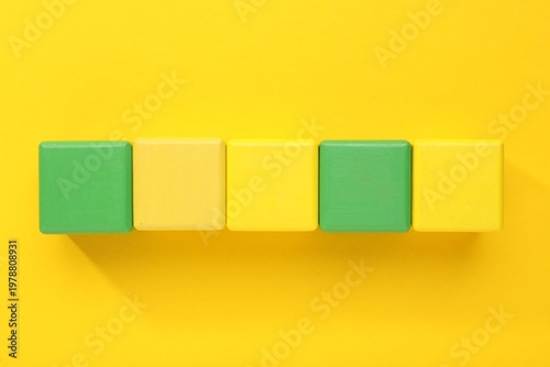 Empty colorful wooden cubes on yellow background, flat lay. Space for text