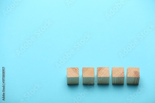Empty wooden cubes on light blue background, space for text