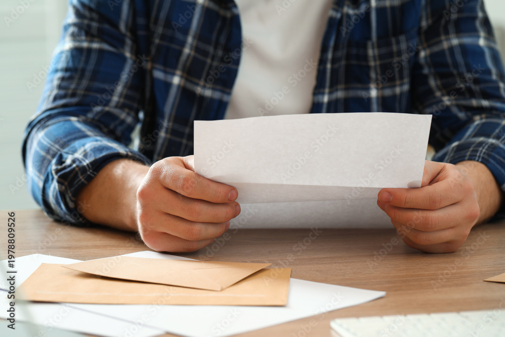 Obraz premium Man reading letter at wooden table indoors, closeup