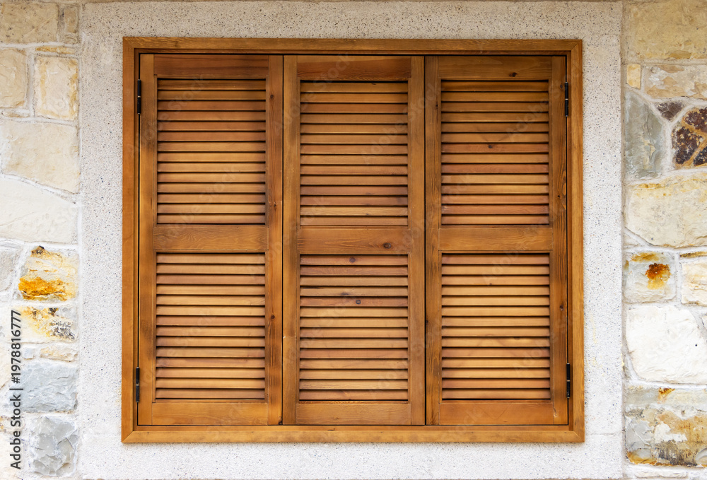 Obraz premium Wooden shutters background of a rustic window with three brown timber louvered panels set in a textured natural stone wall for Mediterranean architectural design.