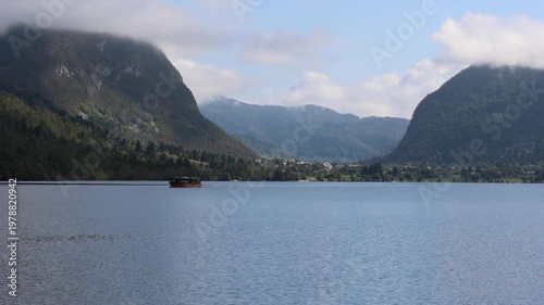 lake bohinj with mountains background (aerial view of famous alpine travel destination in slovenia) boat kayaking scenic european tourism getaway (julian alps, europe) rain view scenic landscape